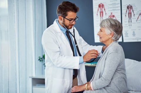 Doctor examining senior patient with stethoscope in clinic