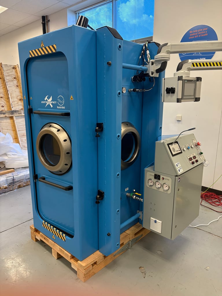Large blue industrial machine with circular ports and control panel mounted on wooden pallet in laboratory setting
