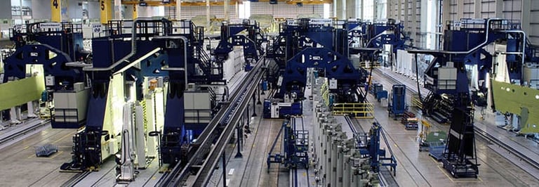 Industrial manufacturing facility with multiple large blue machines and equipment arranged on factory floor with yellow safety barriers